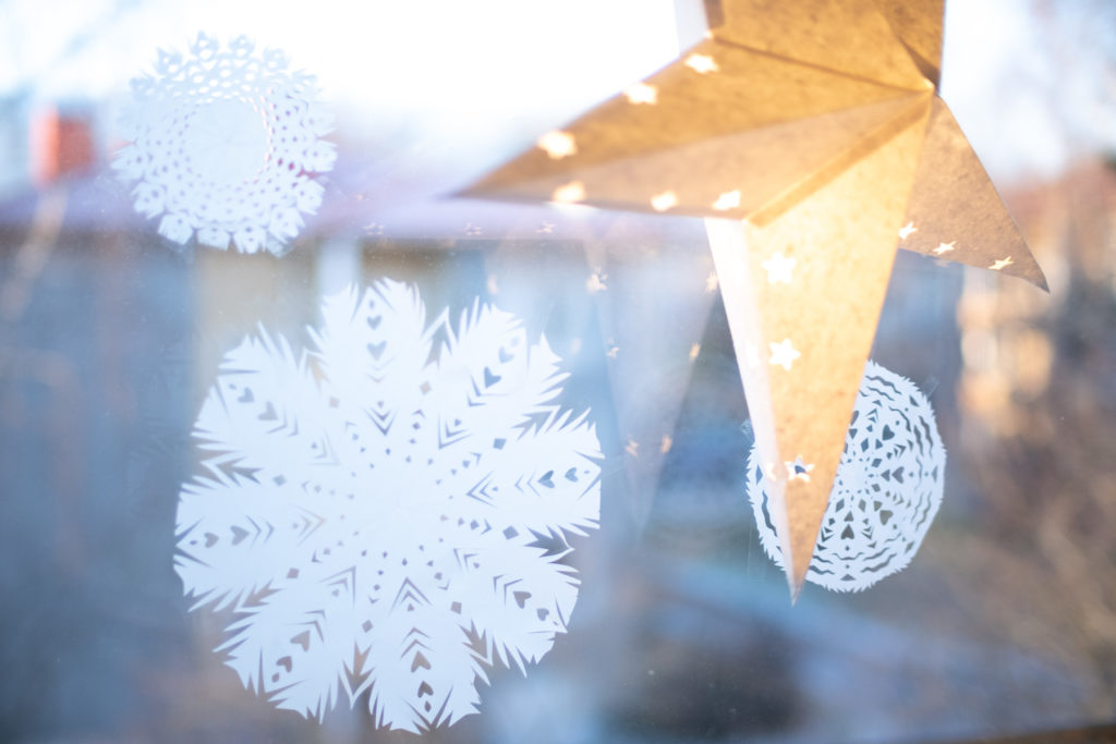 Ikkunassa paperinen tähti ja paperista leikattuja lumihiutaleita
